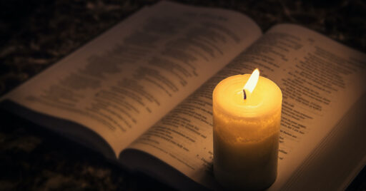 Candle illuminating the Bible in the dark. Is Jesus God